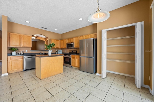 kitchen with ceiling fan, light tile patterned flooring, a kitchen island, decorative light fixtures, and appliances with stainless steel finishes