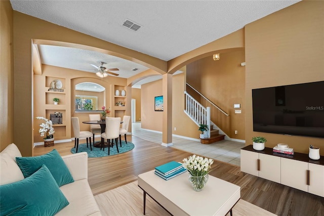 living room featuring a textured ceiling, wood-type flooring, built in shelves, and ceiling fan