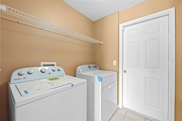 laundry area with a textured ceiling, light tile patterned flooring, and washer and dryer