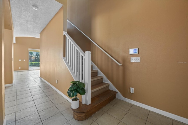 staircase with high vaulted ceiling, a textured ceiling, and tile patterned floors