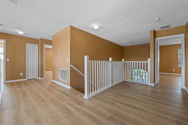 unfurnished room with a textured ceiling and light hardwood / wood-style flooring