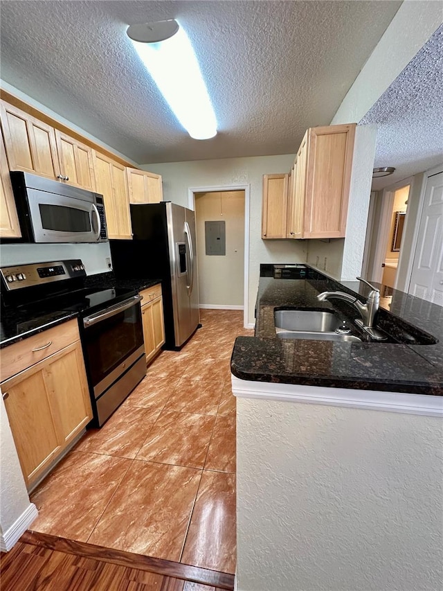 kitchen featuring a textured ceiling, stainless steel appliances, light brown cabinetry, and light wood-type flooring