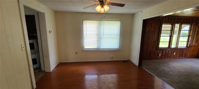 spare room with dark wood-type flooring, ceiling fan, and wooden walls