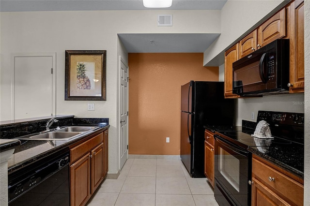 kitchen featuring dark stone counters, black appliances, light tile patterned floors, and sink