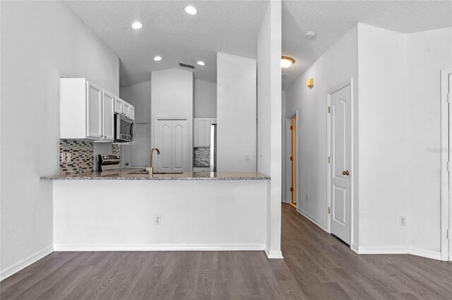 kitchen with light stone countertops, kitchen peninsula, white cabinetry, and stainless steel appliances