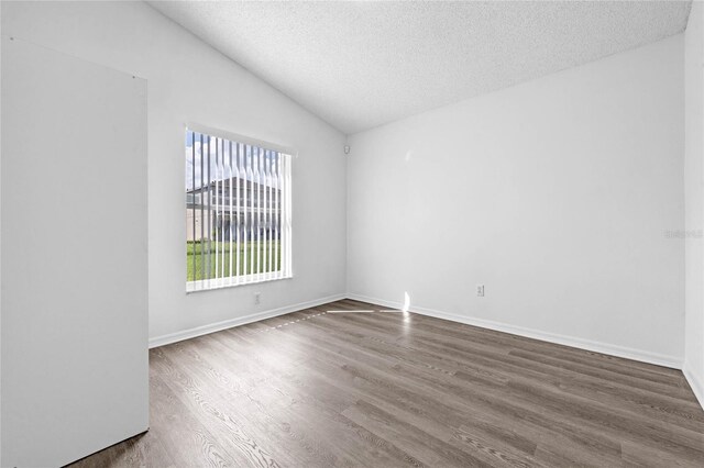 unfurnished room with a textured ceiling, vaulted ceiling, and hardwood / wood-style floors