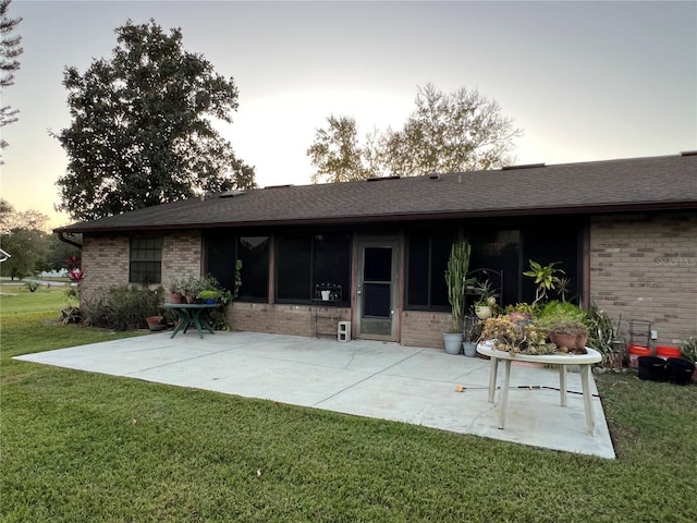 back house at dusk with a patio and a lawn