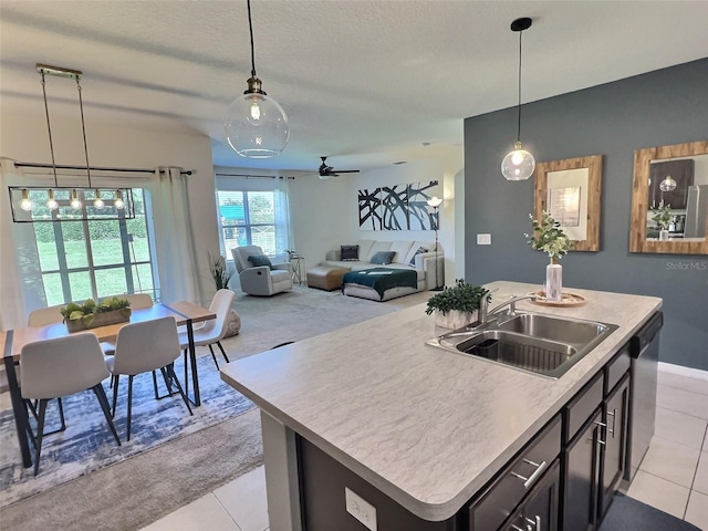 kitchen featuring an island with sink, light tile patterned floors, sink, stainless steel dishwasher, and decorative light fixtures