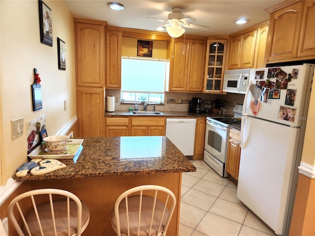 kitchen featuring dark stone counters, light tile patterned flooring, sink, white appliances, and ceiling fan