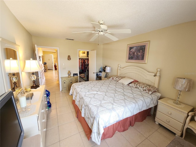 bedroom featuring a closet, a textured ceiling, a walk in closet, light tile patterned floors, and ceiling fan