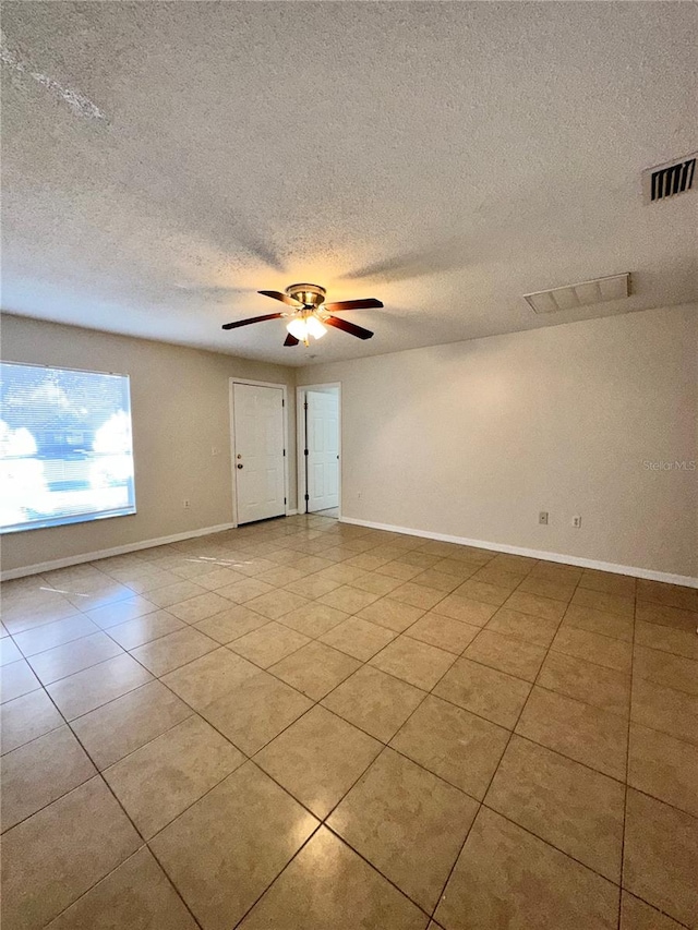 spare room with a textured ceiling, light tile patterned floors, and ceiling fan