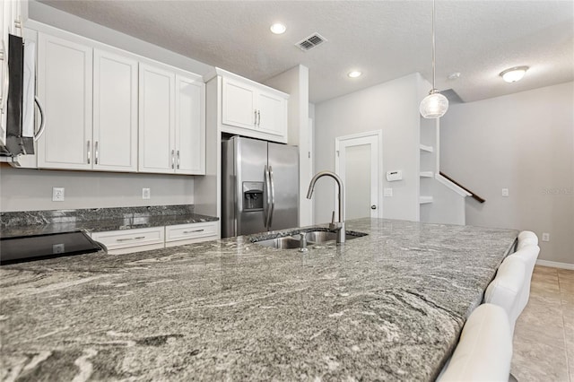 kitchen with appliances with stainless steel finishes, hanging light fixtures, white cabinets, dark stone counters, and sink