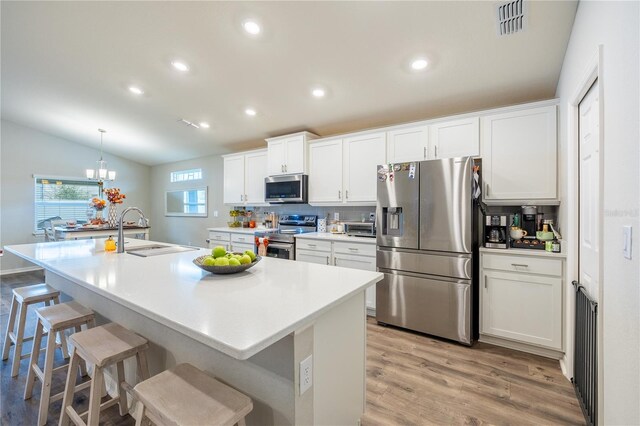 872 Sydney St, Davenport, FL 33837 - kitchen with appliances with stainless steel finishes, a sink, white cabinets, light wood finished floors, and an island with sink