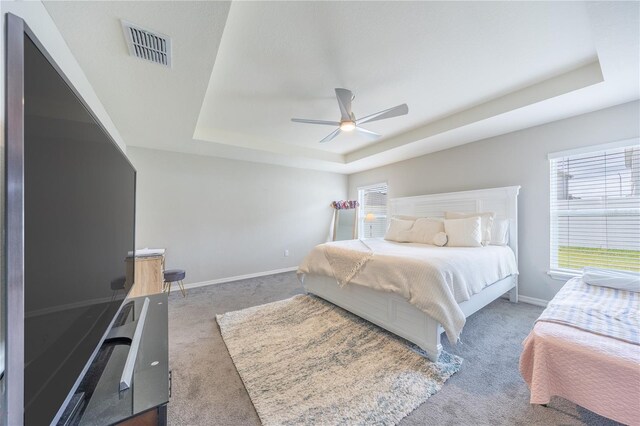 carpeted bedroom featuring ceiling fan and a raised ceiling