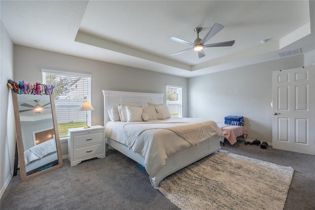 carpeted bedroom with ceiling fan and a raised ceiling