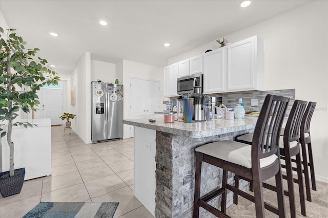 kitchen with kitchen peninsula, white cabinetry, a kitchen breakfast bar, appliances with stainless steel finishes, and decorative backsplash