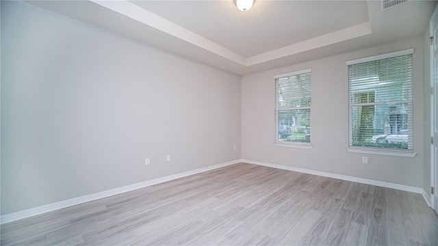 unfurnished room featuring a textured ceiling, light wood-type flooring, and a raised ceiling