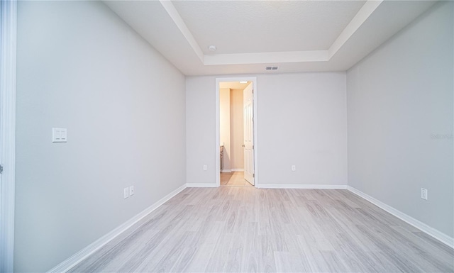 empty room with light hardwood / wood-style flooring and a raised ceiling