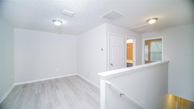 hall with a textured ceiling and light wood-type flooring