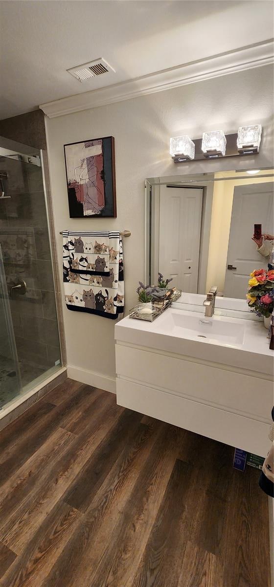 bathroom with vanity, hardwood / wood-style flooring, a shower with shower door, and crown molding