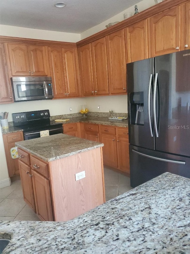 kitchen with light stone counters, appliances with stainless steel finishes, light tile patterned flooring, and a center island