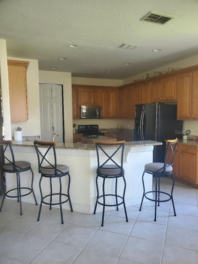 kitchen featuring kitchen peninsula, dark stone countertops, black appliances, and a breakfast bar area