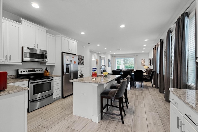 kitchen with white cabinetry, stainless steel appliances, a center island, light stone countertops, and a kitchen bar