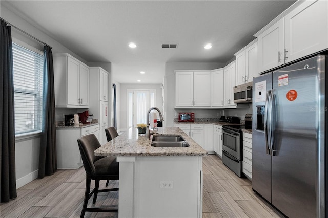 kitchen featuring sink, a center island with sink, white cabinetry, appliances with stainless steel finishes, and a breakfast bar