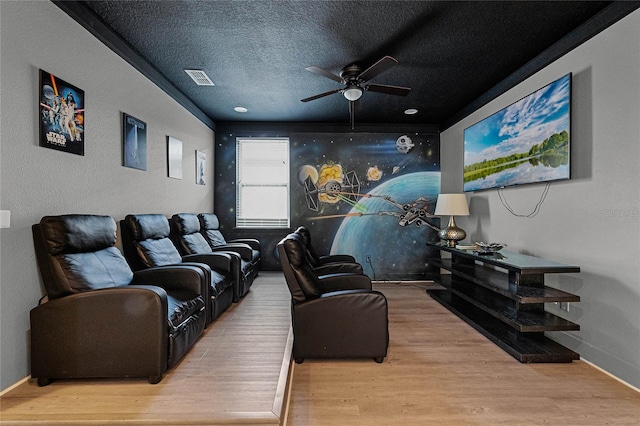 cinema with ceiling fan, a textured ceiling, and light hardwood / wood-style flooring