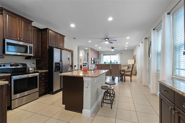 kitchen with light stone countertops, stainless steel appliances, a kitchen bar, and a kitchen island with sink