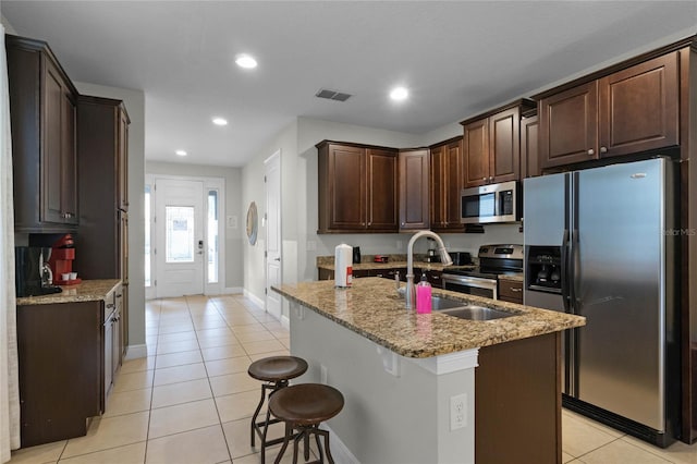 kitchen with light stone counters, an island with sink, sink, stainless steel appliances, and a breakfast bar area