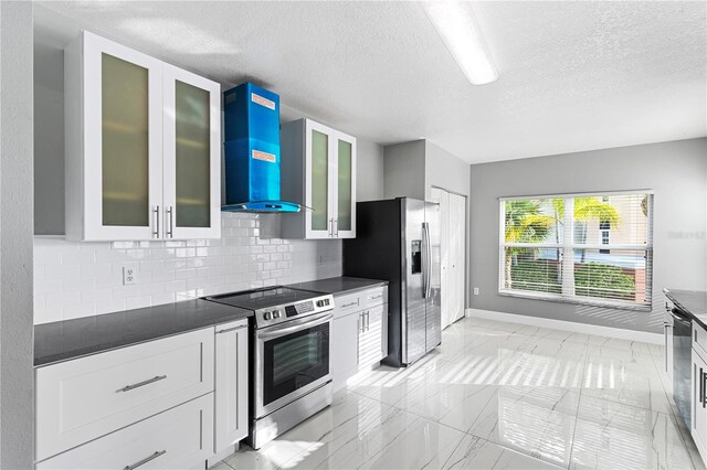 kitchen with a textured ceiling, appliances with stainless steel finishes, wall chimney exhaust hood, and decorative backsplash