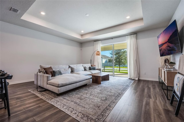 living room with a textured ceiling, a tray ceiling, and dark hardwood / wood-style flooring