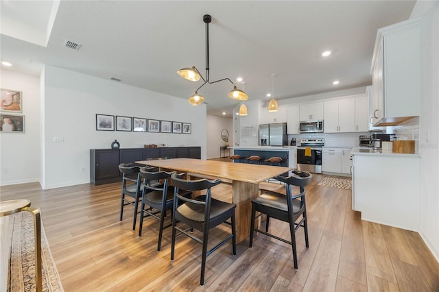 dining room with a notable chandelier, light wood-type flooring, and sink