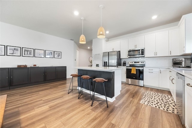 kitchen featuring stainless steel appliances, pendant lighting, a kitchen island, and white cabinetry