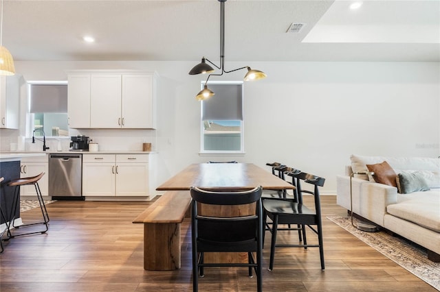 kitchen featuring light hardwood / wood-style floors, decorative light fixtures, stainless steel dishwasher, and white cabinetry