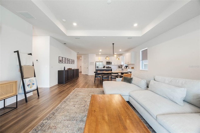 living room with a tray ceiling and dark wood-type flooring