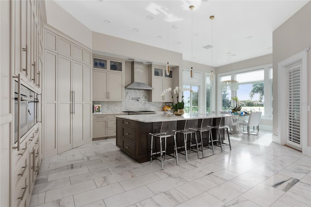 kitchen with decorative backsplash, a spacious island, a kitchen bar, pendant lighting, and wall chimney exhaust hood