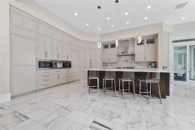 kitchen with a large island with sink, backsplash, a kitchen bar, wall chimney exhaust hood, and decorative light fixtures