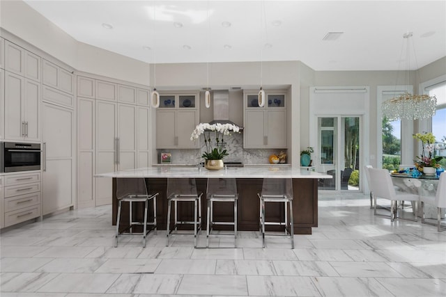 kitchen with wall chimney range hood, decorative backsplash, a large island with sink, a kitchen breakfast bar, and decorative light fixtures