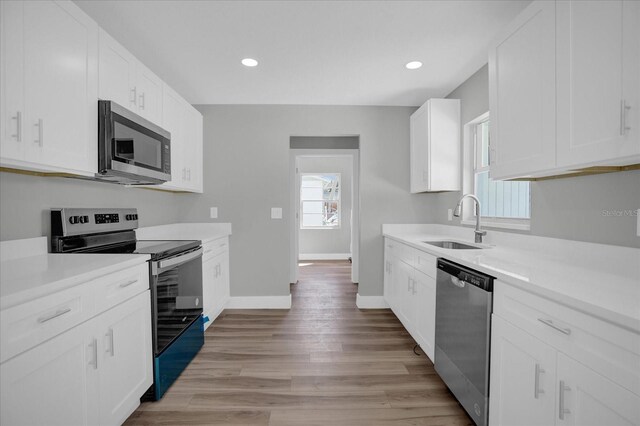 kitchen with sink, light wood-type flooring, white cabinets, and appliances with stainless steel finishes