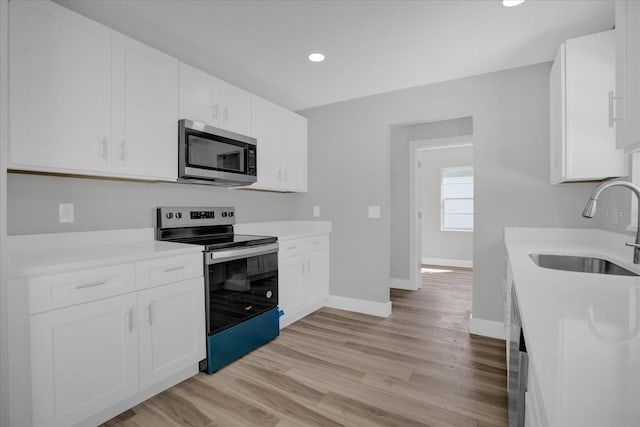 kitchen with sink, stainless steel appliances, white cabinets, and light wood-type flooring