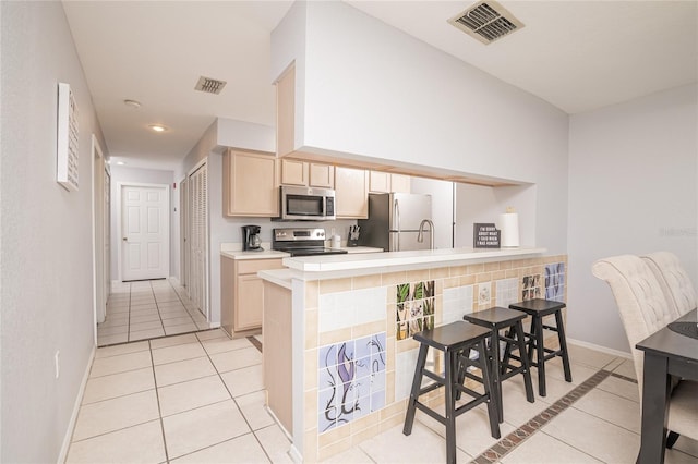 kitchen featuring backsplash, kitchen peninsula, light brown cabinets, light tile patterned floors, and stainless steel appliances