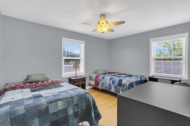 bedroom featuring multiple windows, a textured ceiling, light hardwood / wood-style floors, and ceiling fan