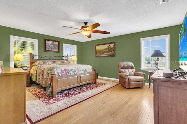 bedroom featuring multiple windows, a textured ceiling, ceiling fan, and light hardwood / wood-style flooring