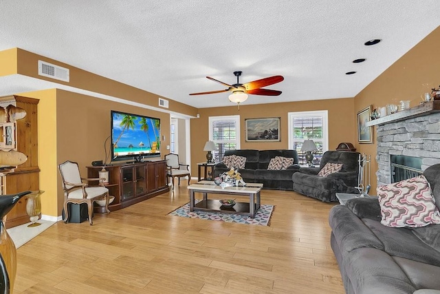 living room with a textured ceiling, a fireplace, ceiling fan, and light hardwood / wood-style flooring