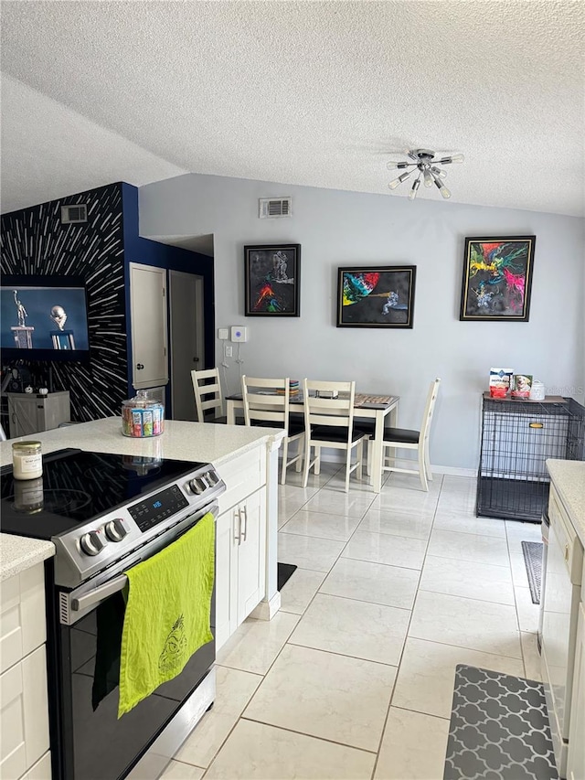 kitchen with a textured ceiling, stainless steel electric stove, light tile patterned floors, and white cabinets