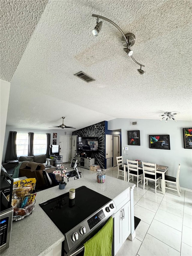 kitchen with a textured ceiling, electric range oven, white cabinetry, and light tile patterned floors