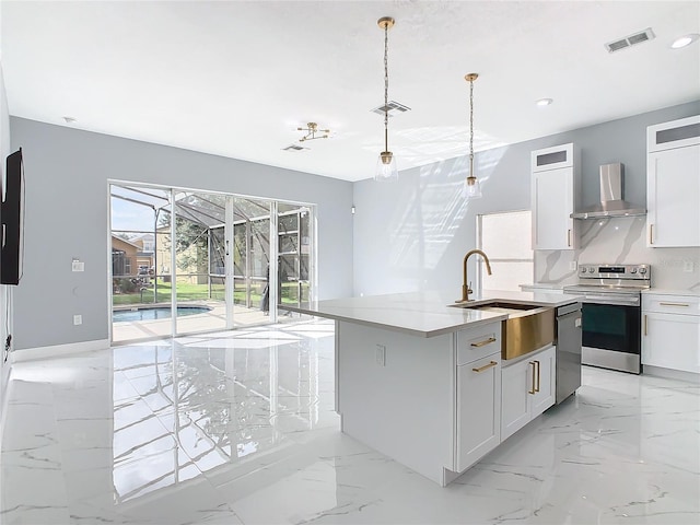 kitchen featuring wall chimney range hood, sink, white cabinetry, stainless steel appliances, and a center island with sink