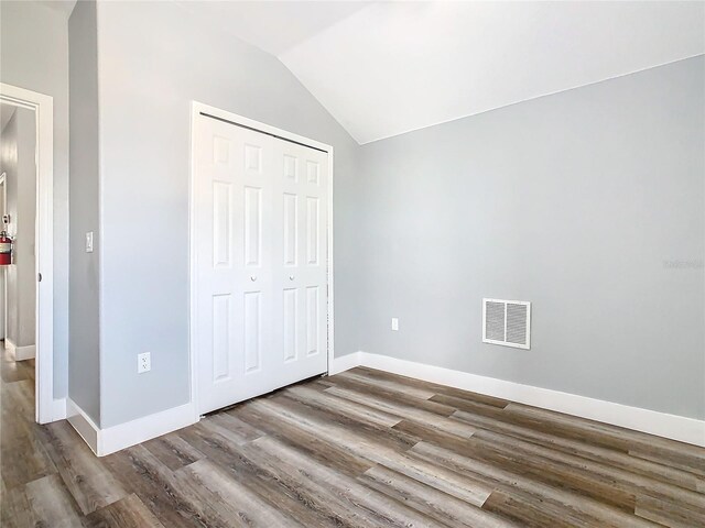 unfurnished bedroom with a closet, wood-type flooring, and lofted ceiling